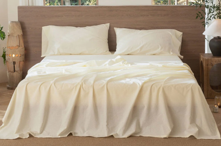 bed with a flat sheet draped loosely over the mattress and pillows