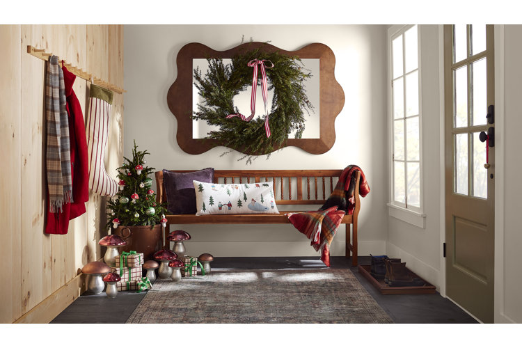entryway with a large green christmas wreath on top of a mirror surrounded by christmas decor and a bench