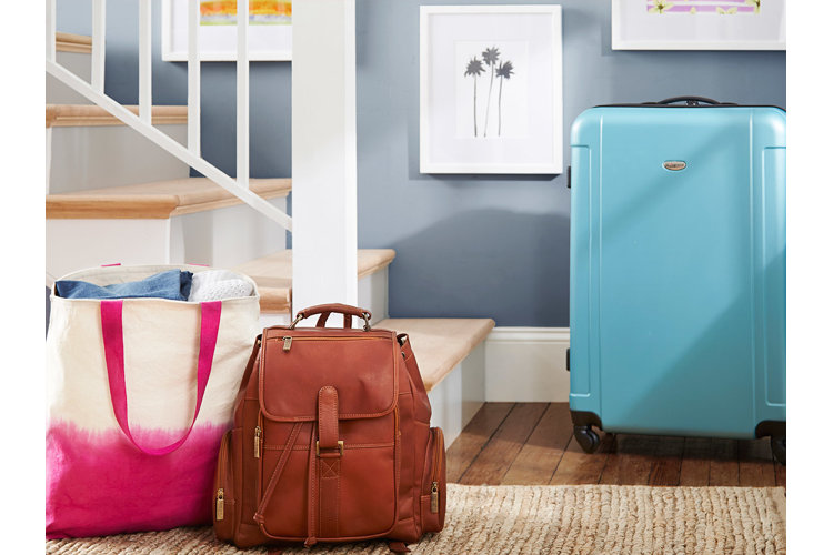 Packed tote bag, leather backpack and blue suitcase near a staircase