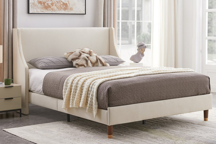 bed with beige upholstered frame, gray quilt, and soft cream throw blanket