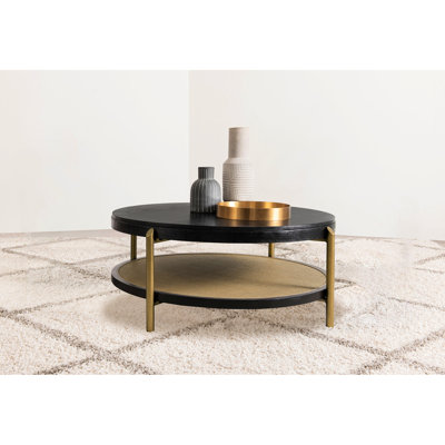 Table basse ronde noire autoportante avec tablette de rangement et pieds en laiton vieilli, idéale pour les espaces de vie. Fabriqué en hévéa, en bois d'ingénierie et en placage de frêne blanc, avec un plateau inférieur en bois tressé naturel.