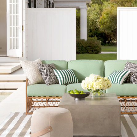 Outdoor patio setup with a light green couch, striped pillows, and square coffee table.