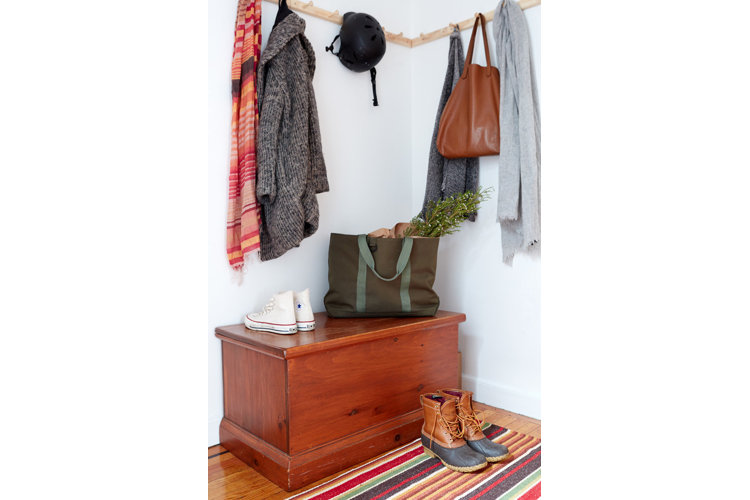 An entryway with wall-mounted coat hooks and a wooden storage bin.