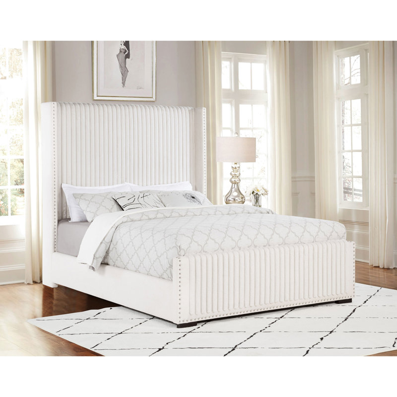 Grand lit tapissier en tissu crème avec oreilles, capitonnage vertical et profil bas pour chambre à coucher crème, garniture cloutée, support stable