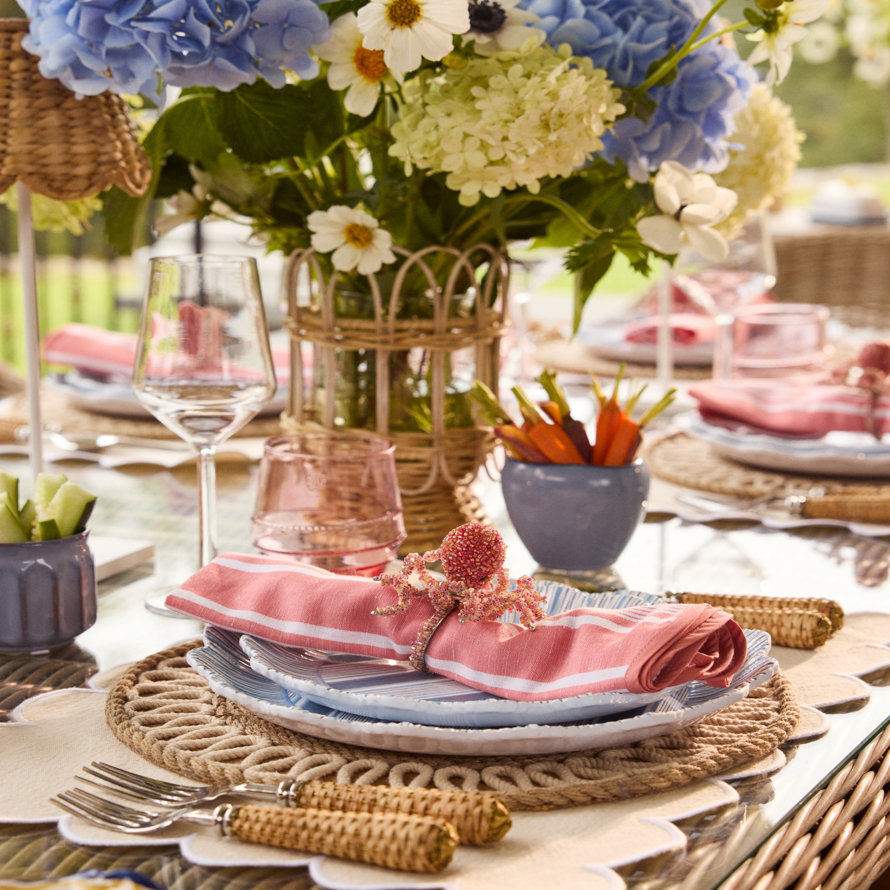 A table setting with blue and white dishes, pink striped napkins, and a floral centerpiece.