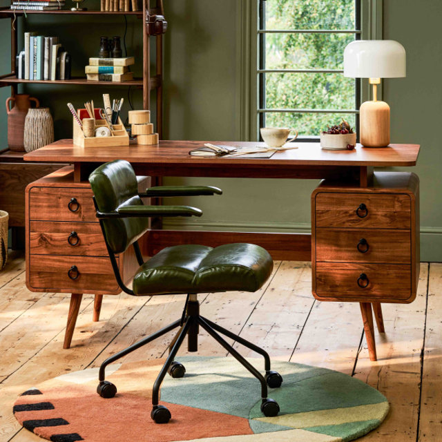 A mid-century modern wooden desk with two pedestal drawer units and a green faux leather office chair on a circular geometric rug in a home office.