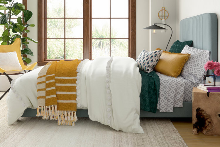 bright modern boho bedroom with a blue upholstered bed, gray patterned sheets, textured white duvet cover, and a striped yellow throw blanket