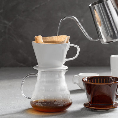 Ceramic pour-over coffee dripper cone sitting on a glass carafe