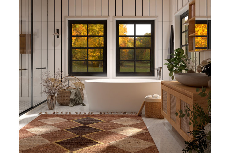 Country cottage bathroom with wood vanity. Brown rug next to a white bath and plenty of woven baskets. A range of live and dried flowers