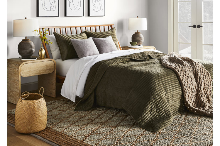 neutral bedroom with a green quilt and brown knit weighted blanket on a wood bed