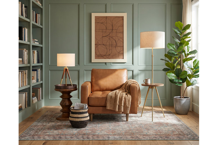 transitional-style reading nook with sage green board and batten walls, built-in floor-to-ceiling bookcases, a leather armchair, and two modern end tables
