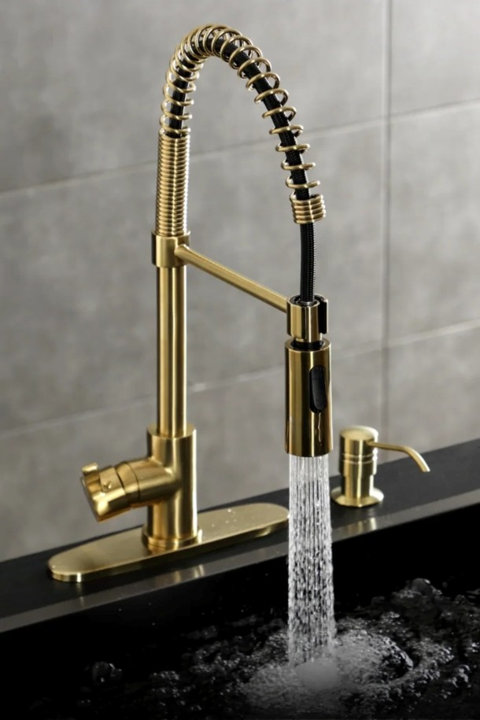 Brushed gold pull-down kitchen faucet with a black coil spring neck and matching soap dispenser pouring water into a black sink.