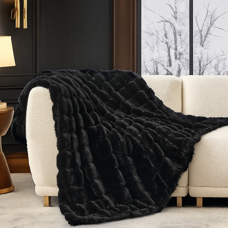 Black faux fur throw blanket with a wide striped texture draped over a cream sofa