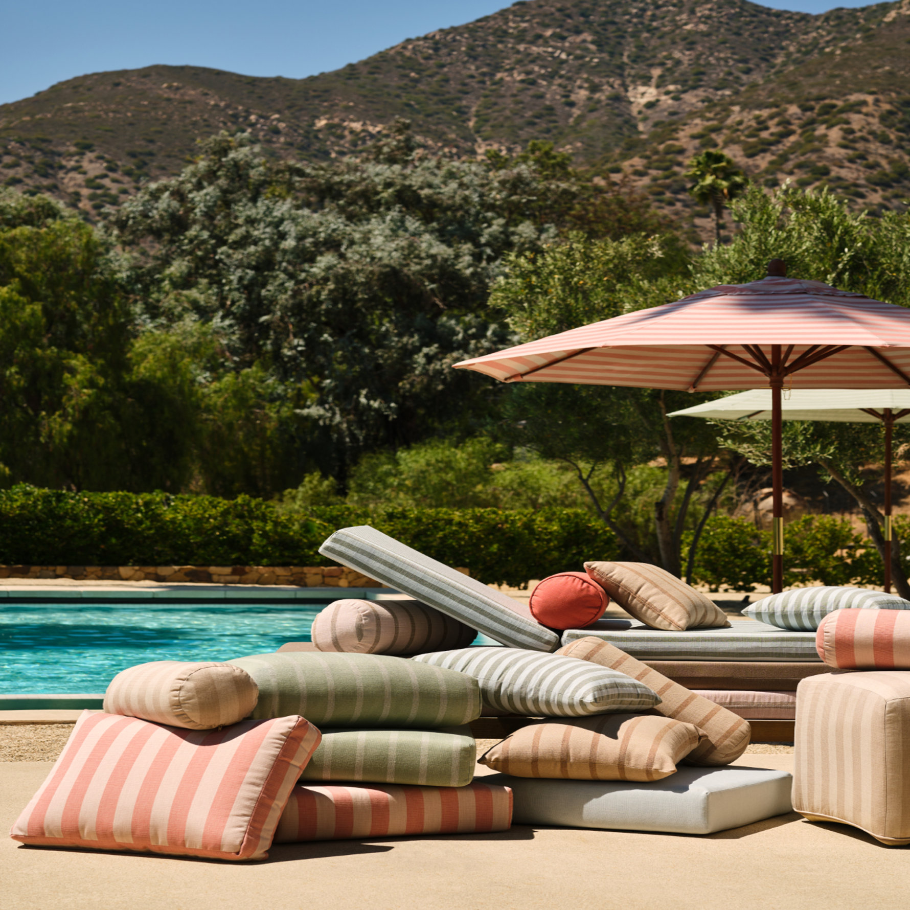 Outdoor striped pillows, loungers, and umbrellas next to a pool.
