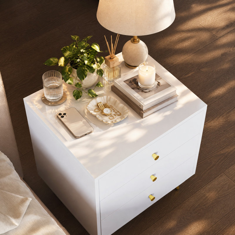 Table de chevet moderne et glamour à 3 tiroirs de 50 cm de large, avec pattes et poignées en métal doré.