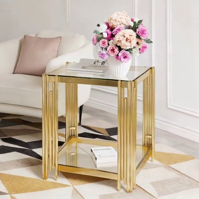 Table basse moderne en verre transparent avec structure asymétrique en métal, finition dorée et tablette inférieure pour un rangement élégant