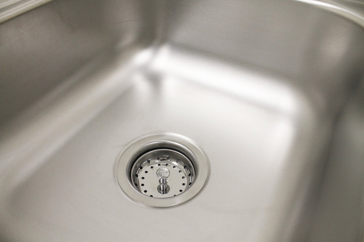 Close-up of a stainless steel sink with a round sink drain and a strainer basket.