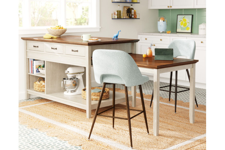 Kitchen island with wood top and pull-out breakfast table. Two blue upholstered chairs with wood legs. Woven area rug