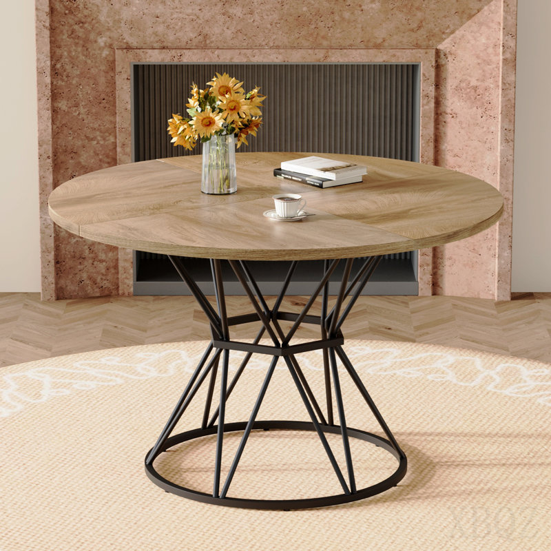Une table de salle à manger circulaire d'un diamètre de 47,3 pouces, comprenant 4 plateaux de table en MDF à grain de bois clair, des supports en métal en forme de sablier noir et une table de salle à manger de style industriel moderne pour 4 à 6 personnes.