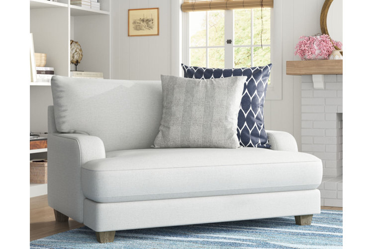 A white low-profile chair-and-a-half armchair in the corner of a living room and decorated with a pair of throw pillows