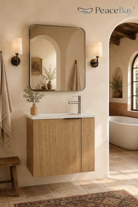 Modern wall-mounted bathroom vanity with a light oak finish, white countertop, and brushed nickel faucet, positioned beneath a rounded rectangular mirror and flanked by sconces in a rustic, arched bathroom with terra cotta tile flooring and a freestanding tub.