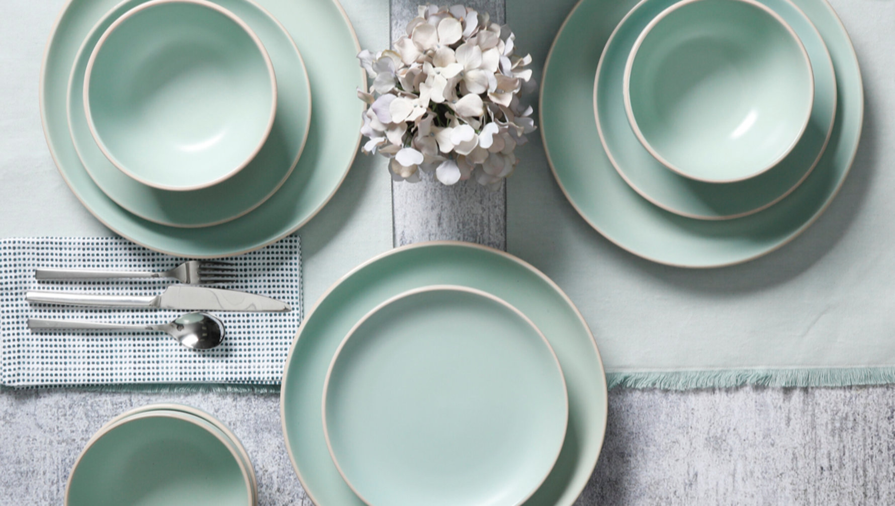 Overhead view of mint dinnerware with flatware and a floral centerpiece.