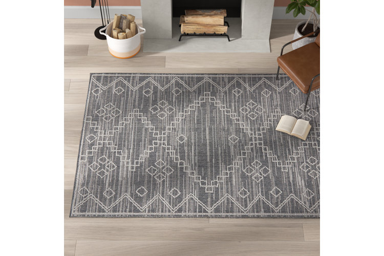 gray and white geometric patterned area rug in front of a fireplace with a brown leather accent chair on top of it