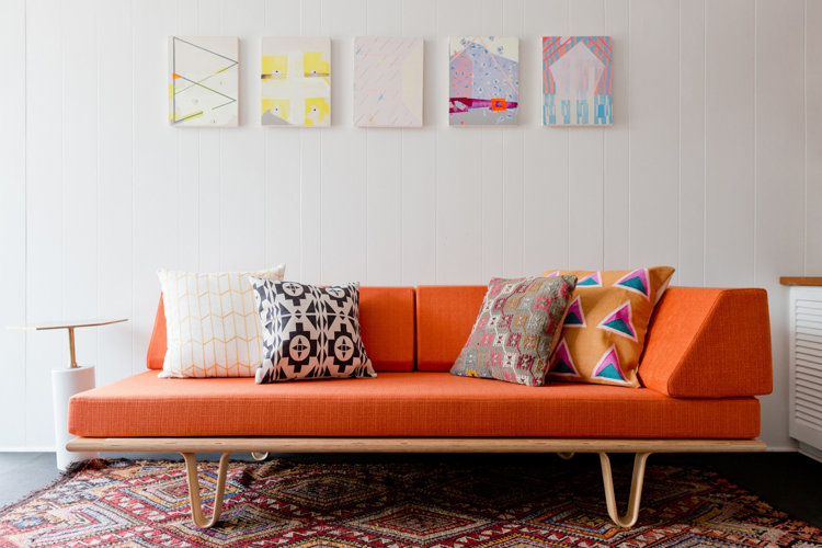 Orange sofa with colorful pillows and wall art hanging above.