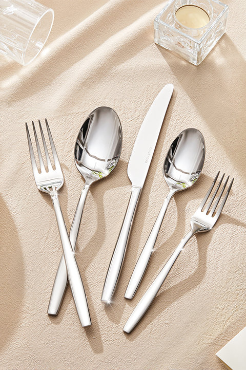 Polished stainless steel silverware set including a dinner fork, dinner spoon, dinner knife, teaspoon, and salad fork arranged on a beige textured tablecloth.