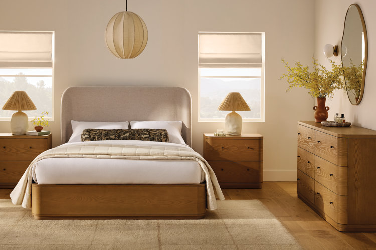 Boho bedroom with light wood furniture, an upholstered wingback-style headboard, pleated table lamps, and a paper globe pendant light