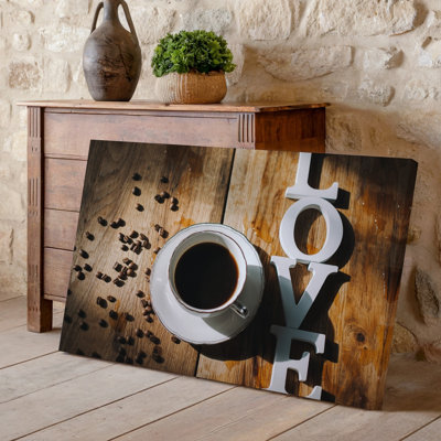 Toile vue de haut en bas d'une table en bois avec art mural, tasse à café blanche remplie de café foncé, position centrale