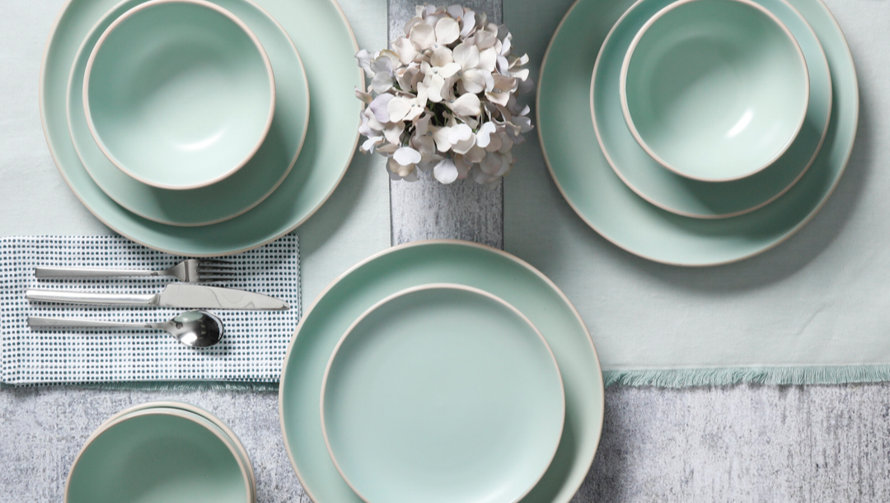 Overhead view of mint dinnerware with flatware and a floral centerpiece.