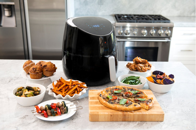 air fryer on a counter in front of an oven surrounded by plates of food