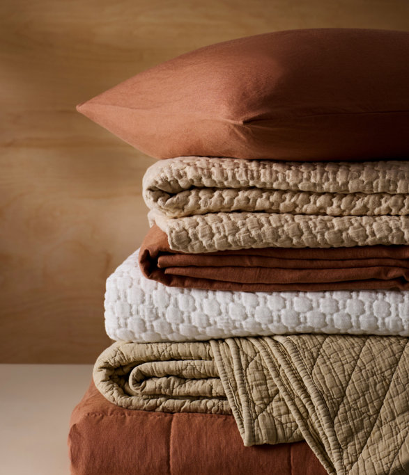 A stack of folded quilts and a pillow.