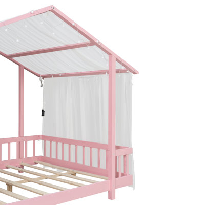 Lit plateforme avec auvent en tissu transparent et guirlandes de lumières, structure en bois en forme de maison avec garde-corps
