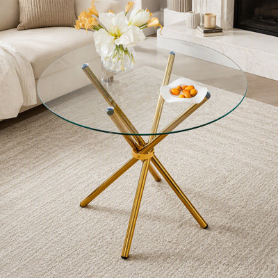 Table de salle à manger ronde en verre transparent pour 4 à 6 personnes avec pieds en métal doré en forme d'anneau, idéale pour les cuisines et salles à manger modernes.