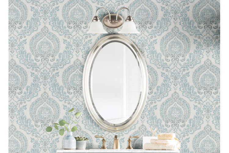 bathroom vanity with downward facing bath sconces, blue wallpaper, and an oval vanity mirror