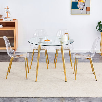 Une table ronde en verre trempé transparent de style minimaliste moderne avec des pieds en métal doré, jumelée à 4 chaises de salle à manger transparentes de style moderne pour une expérience luxueuse