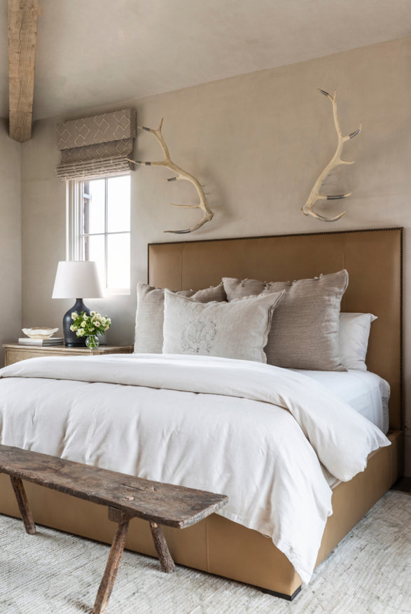 Bedroom with upholstered headboard, antlers, and wood bench.