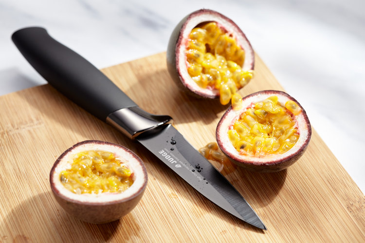 a paring knife on a cutting board next to a freshly sliced passionfruit