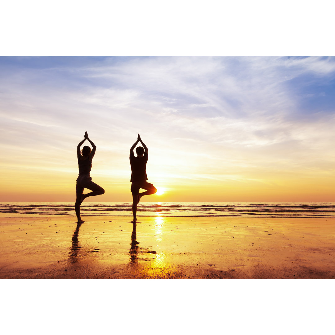 Leinwandbild Zwei Menschen üben Yoga Baum Position am Strand, Sonnenuntergang