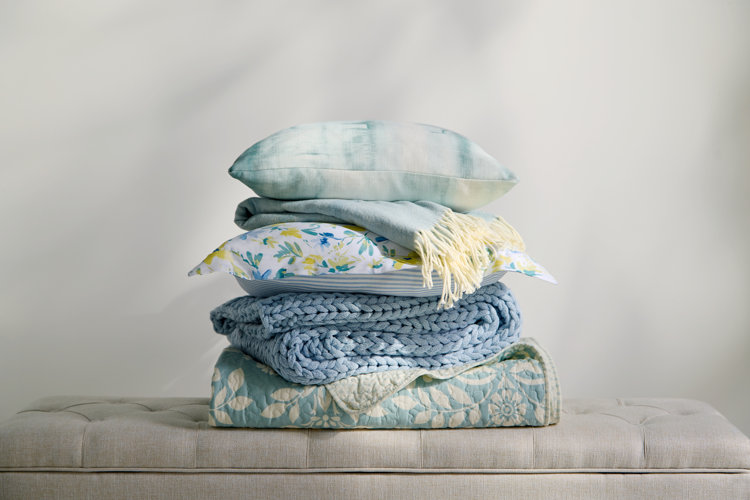 Boho dining room accent textiles including a stack of light blue pillows, a chunky knit throw, and floral patterned quilts