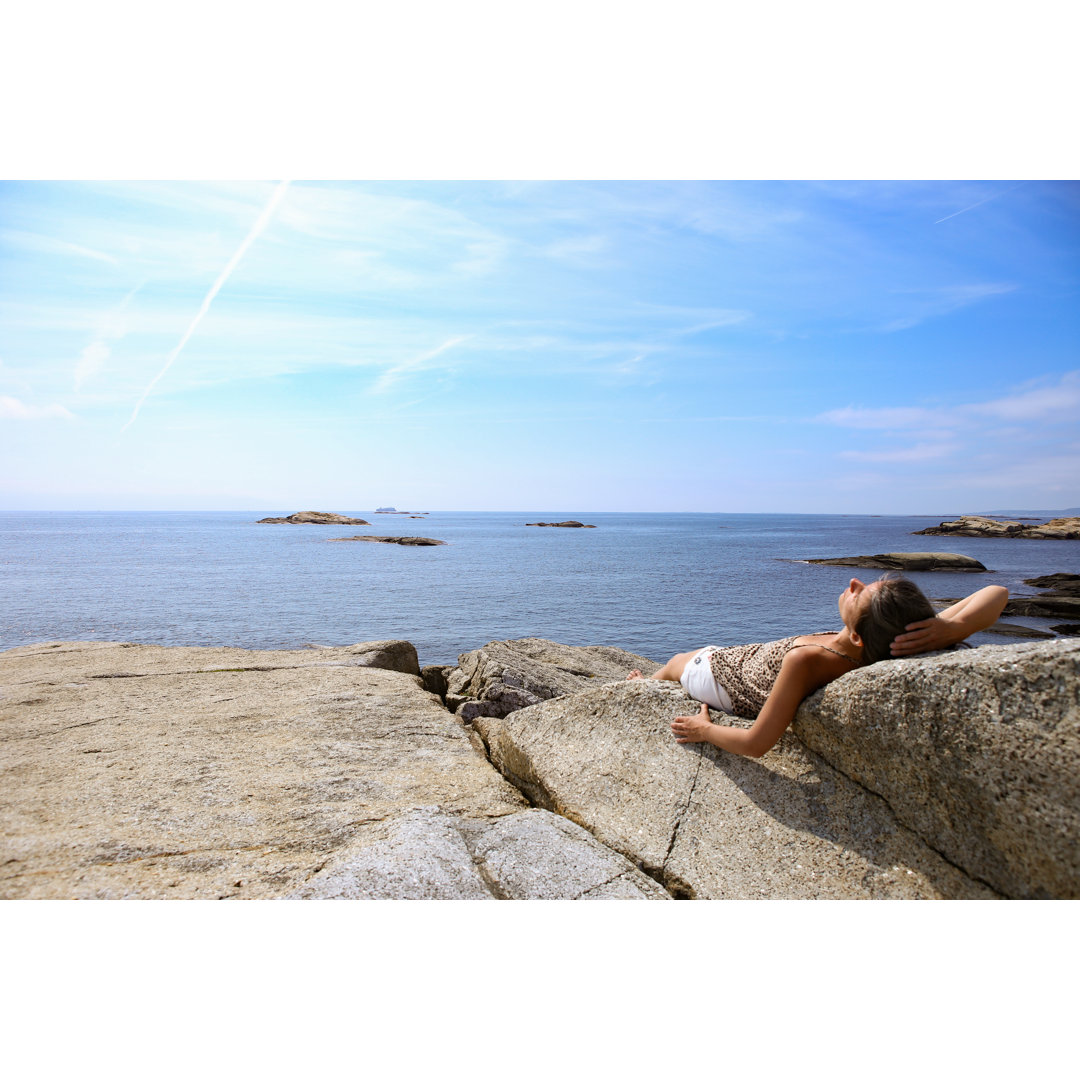 Leinwandbild Frau beim Sonnenbaden auf einem Felsen am Ende der Welt in Norwegen