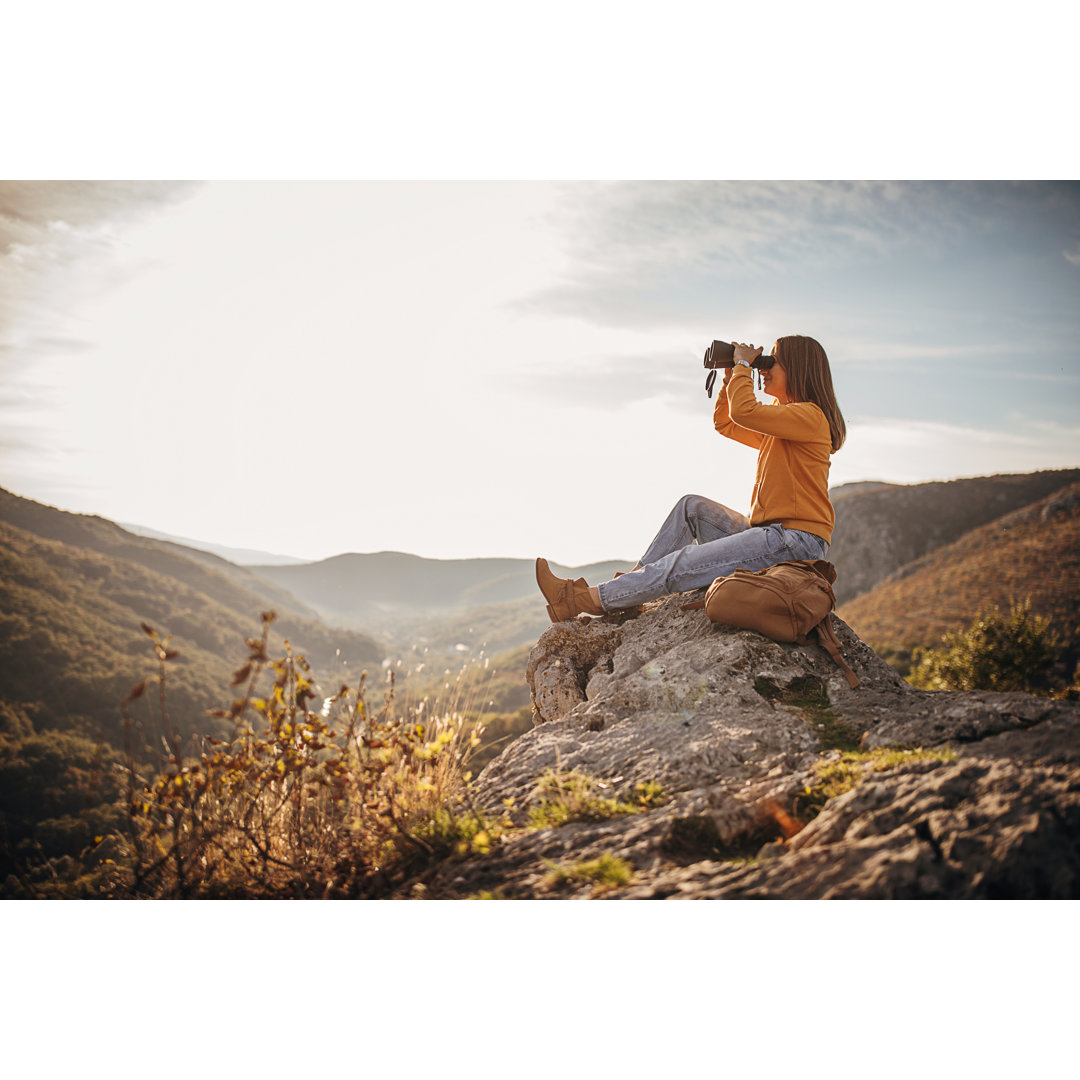 Frau mit Fernglas auf Berggipfel bei Sonnenuntergang by South_agency - No Frame Print on Canvas