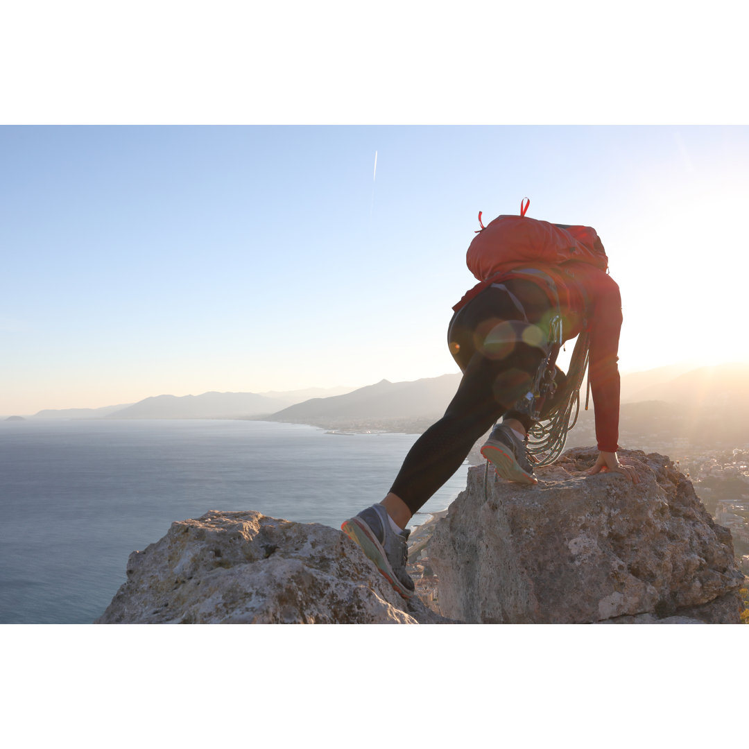 Bergsteigerin streckt sich bei Sonnenuntergang über die Felsen des Gipfels