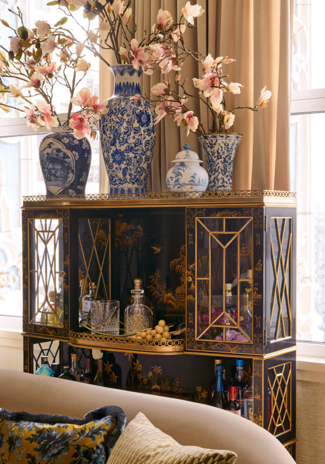 Black and gold bar cabinet decorated with blue and white vases of flowers.