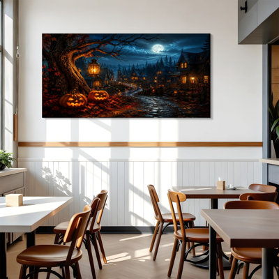Tableau sur toile représentant un village d'Halloween hanté avec des lanternes lumineuses et la pleine lune. Décoration murale idéale pour le salon, la salle de bain, la chambre à coucher ou le bureau. Dimensions : 61 cm (H) x 122 cm (L). Prêt à accrocher.