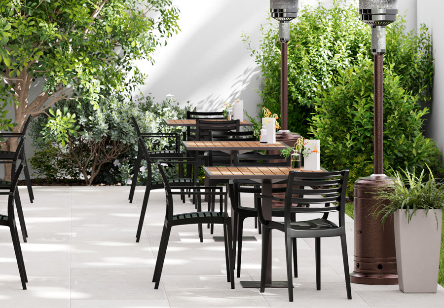 3 outdoor restaurant tables with matching chairs on a restaurant patio in a wooden color and black. Surrounded by plants and heat lamps.