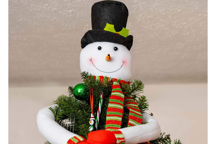 Snowman head with a top hat, striped scarf, and carrot nose on top of a Christmas tree with a pair of arms wrapped around it.
