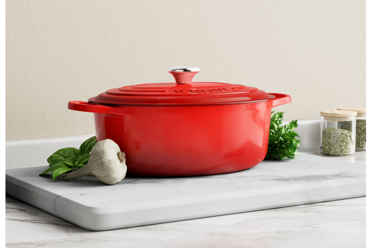 Red dutch oven on a marble cutting board on a marble countertop.